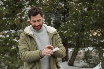 Obraz premium Man applying cream from tube onto hand outdoors, space for text. Winter care