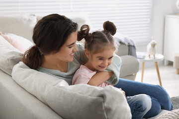Fototapeta premium Young mother and her daughter spending time together on sofa at home