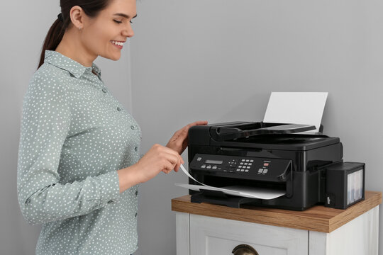 Woman Using Modern Printer On Chest Of Drawers At Home