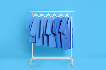 Medical uniforms on rack against light blue background