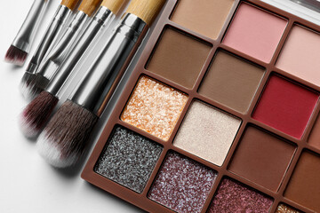 Beautiful eye shadow palette and brushes on white table, flat lay