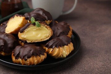 Delicious profiteroles with chocolate spread and cream on textured table, closeup. Space for text