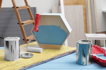 Cans of paint, roller and tray on blue wooden table indoors