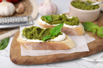 Tasty bruschettas with cream cheese, pesto sauce and fresh basil on white table, closeup