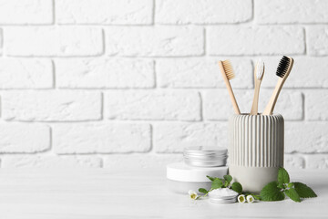 Toothbrushes, dental products and herbs on white wooden table. Space for text