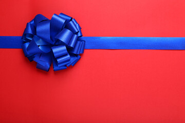 Blue ribbon with bow on red background, top view. Space for text