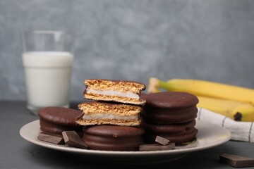 Plate with tasty banana choco pies and pieces of chocolate on grey table, closeup. Space for text