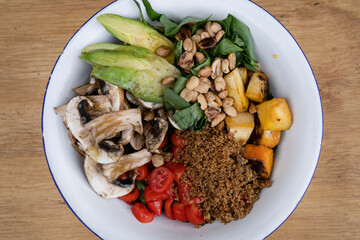 Vegan cuisine. Top view of a fresh salad, with sliced avocado, grilled pumpkin, quinoa, mushrooms, cherry tomatoes and roasted chestnuts, in a white bowl on the wooden table.