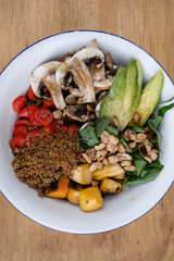 Vegan cuisine. Top view of a fresh salad, with sliced avocado, grilled pumpkin, quinoa, mushrooms, cherry tomatoes and roasted chestnuts, in a white bowl on the wooden table.