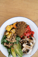 Top view of a fresh salad in a white bowl on the wooden table.