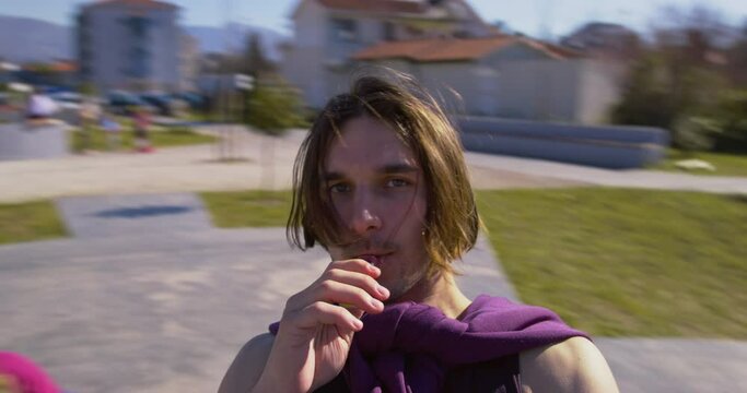 Man in hand holds electronic cigarette, smokes vape enjoys freedom, sunny day, youth. Portrait of guy with caret walks around city, shoots himself on camera blue sky, mountains. Hipster hitchhiking