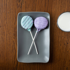 Colorful homemade cake pops on a gray plate with a glass of milk.