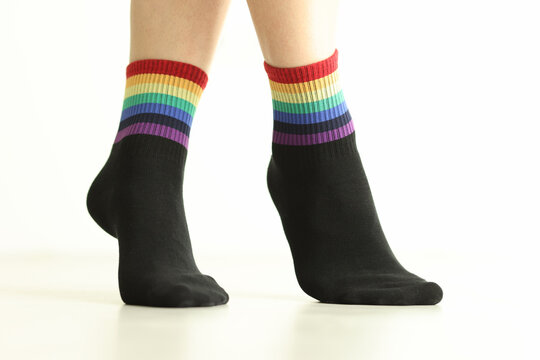 Person wearing black socks with LGBTQ flag decor on white