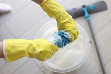 Janitor in rubber gloves wrings mop rag over bucket - obrazy, fototapety, plakaty