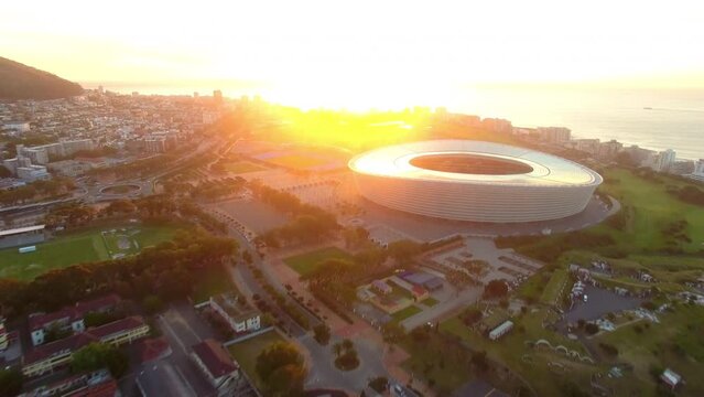 Sunset, stadium and travel with drone of city of cape town for luxury, shopping mall and ferris wheel at sea. Mountains, tourism and landscape with location for retail, vacation and skyline at coast