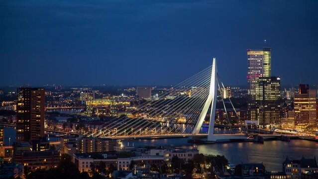 A beautiful timelapse of Rotterdam's skyline and Erasmus Bridge in the Netherlands. This autumn evening showcases a cloudy atmosphere as the city lights illuminate the scene.