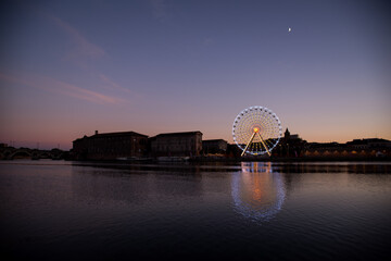Nightly view of a spinning ferris wheel in Toulouse, landscape river and buildings
