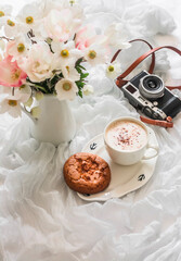 Cozy slow morning in bed - a bouquet of flowers, peanut butter cookies and cappuccino. Lifestyle concept