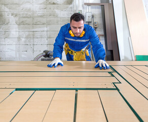Production line atmosphere in a wooden furniture factory. Young technician in blue mechanic...