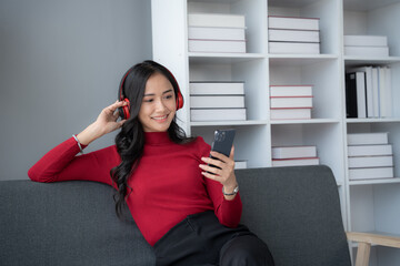 Young charming Asian woman listening to the music while sitting on the sofa in her free time.