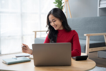 beautiful Asian girl wearing red sweater working with laptop computer in the living room.
