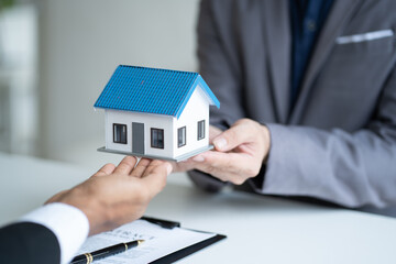 Close up view of real estate agent, and insurance salesman handing over a sample house to a client after signing the sale at the office.