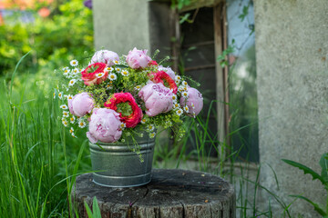 Blumenstrauss mit Pfingstrosen und Rosen in Rosa und Pink auf einem Holzstamm im Garten, natürlich...
