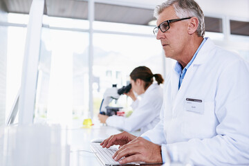 Scientist, man and computer in science research, experiment or data results at laboratory. Senior male typing in medical healthcare working on pc or technology in forensic or scientific lab for cure