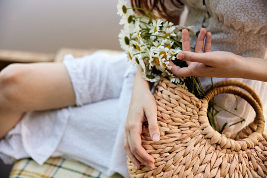 a woman gently touches the daisies lying in a wicker bag. photograph without a face