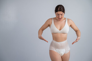 Portrait of a woman pointing at adult diapers on her. Urinary incontinence problem.
