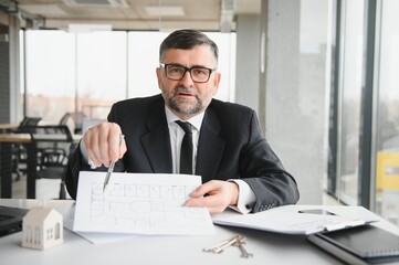 Realtor in suit sitting at desk in office. Realtor is showing apartment.