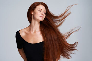 Hair, beauty and woman in studio with wind for keratin treatment, wellness and haircare on gray background. Salon, hairdresser and face of ginger female model for shine, healthy and natural hairstyle