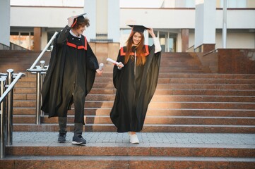 Happy friends on graduation day. Portrait of two cheerful joyful students standing near university...