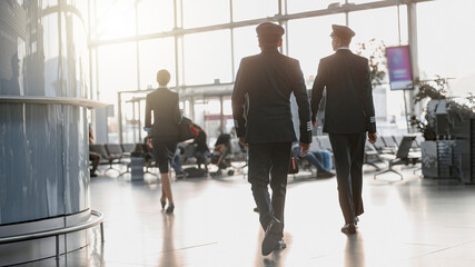 Two pilots walking along the airport terminal following the stewardess © Friends Stock