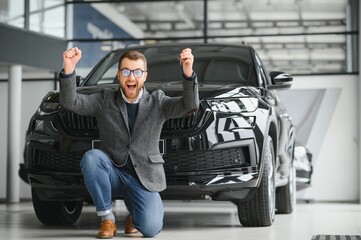 Happy owner of a new car. Emotional handsome man in casual clothes is happy, buying a car in the dealership.