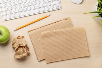 Top view of blank notepad, keyboard, apple and crumpled papers