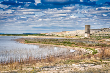 Fototapeta na wymiar The grandiose architecture of San Angelo State Park in Texas rises out of the lush marshlands, its history visible against a shimmering lake and horizon full of fluffy clouds.