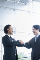 Fototapeta premium Successful business image of shaking hands, contract signing, cooperation, etc. Cool Asian man in a suit vertical backlight