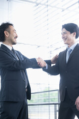 逆光の中、握手をして契約成立や協力など、ビジネスの成功イメージ...