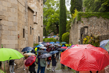 Girona, Spain - May 13th, 2023: TEMPS DE FLORS - Flower Time. Crowd of tourists walking with umbrellas through Old Town on a rainy day through Archaeological Park, Cathedral Gardens and Arab Baths..