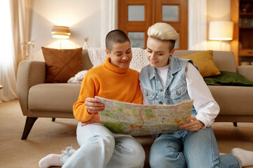 Happy young lesbian woman couple looking at paper map planning trip