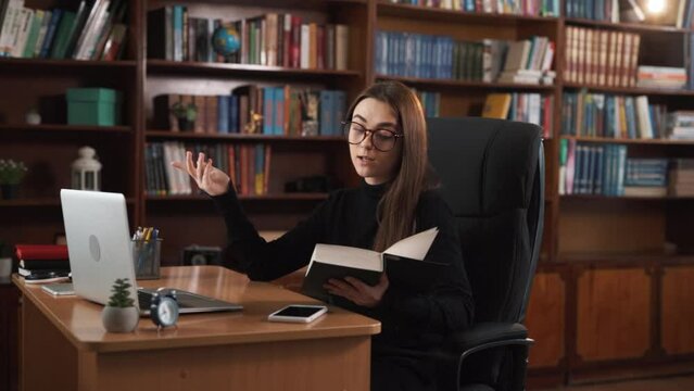 The girl engages in online communication through a webcam while sitting at her desk. She displays a book, reads selected excerpts from it with emotions, and explains their meaning.