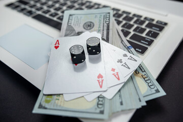 dollar bills and casino dice and cards on laptop keyboard isolated on black background.