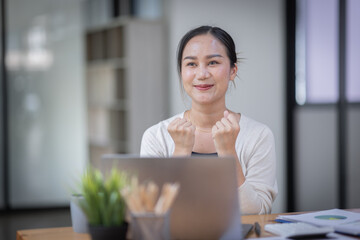 Happy excited successful business asian woman triumphing in office, Portrait of a cheerful Asian businesswoman sitting at the table in office,
