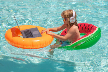Online working and relax in pool. Child relaxing in the pool with laptop. Kid online working on laptop, swimming in a sunny turquoise water pool.
