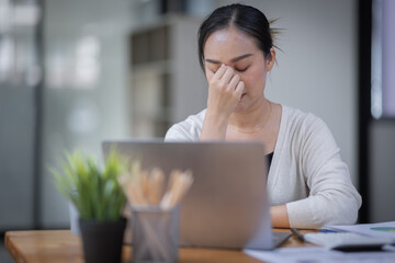 Portrait of tired young business Asian woman work with documents tax laptop computer in office. Sad, unhappy, Worried, Depression, or employee life stress concept
