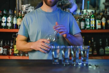 Barman pouring hard spirit into glasses for two male friends relaxing in a bar