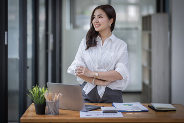 Excited Happy Asian young woman using phone and laptop sitting on a desk office in the day at office	