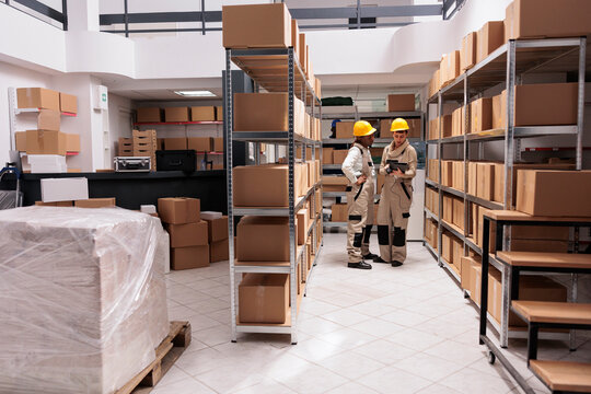 Industrial warehouse employees scanning goods barcodes and tracking parcel in tablet software. Two distribution workers supervising products storaging and using inventory management system app