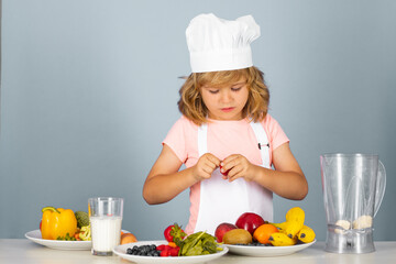 Child wearing cooker uniform and chef hat preparing vegetables on kitchen, studio portrait. Cooking, culinary and kids food concept.